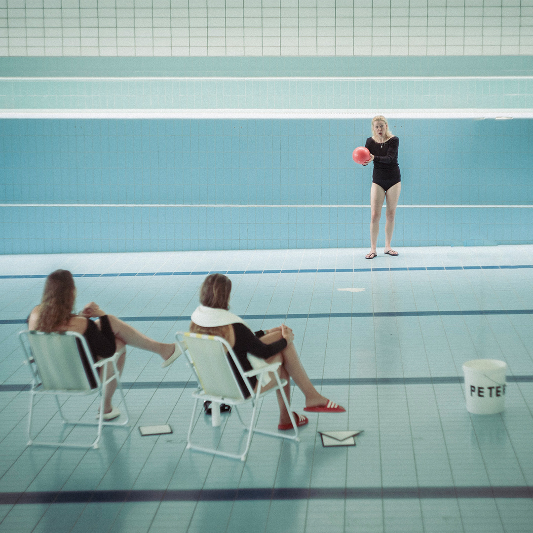 Kaksi ihmistä seuraa, kun kolmas pitelee punaista palloa uimahallissa.