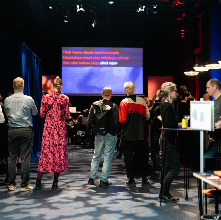 Ihmisiä seisoo Bar Juorussa seuraamassa ohjelmaa.