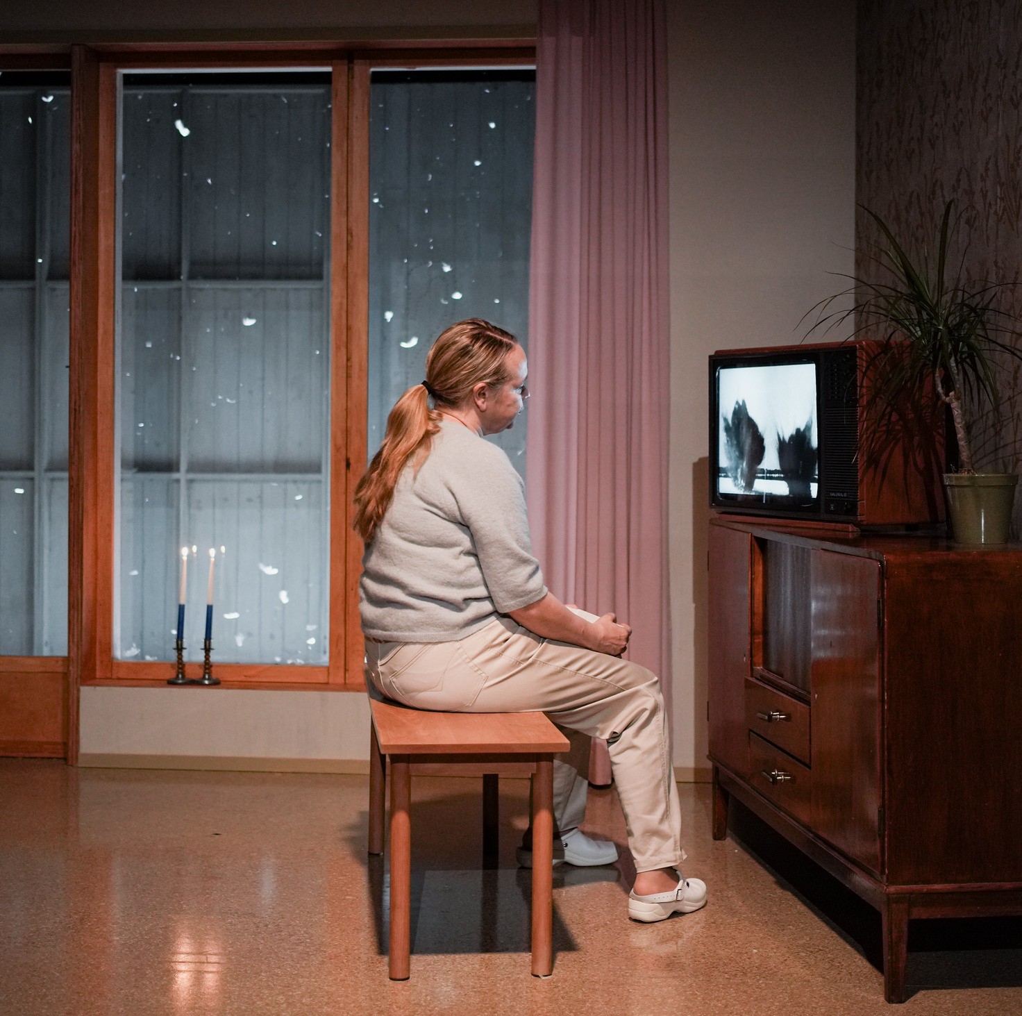 Näyttelijä Katja Kuttner istuu tuolilla ja katsoo mustavalkoista televisiota.