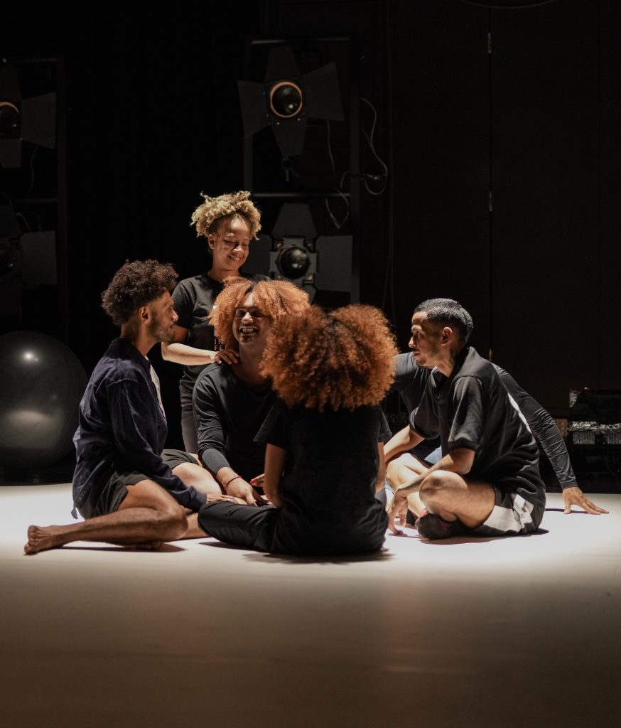 Ryhmä ihmisiä istuu lattialla näyttämöllä.