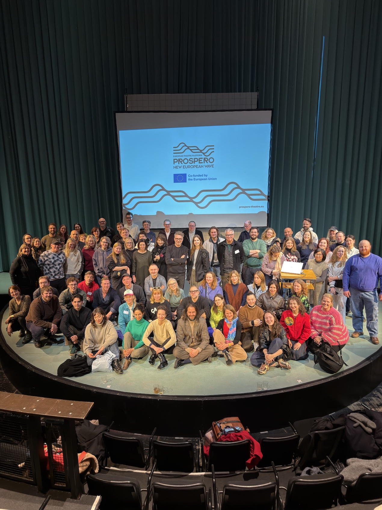 Iso ryhmä ihmisiä istuu ja seisoo lavalla kohti kameraa.