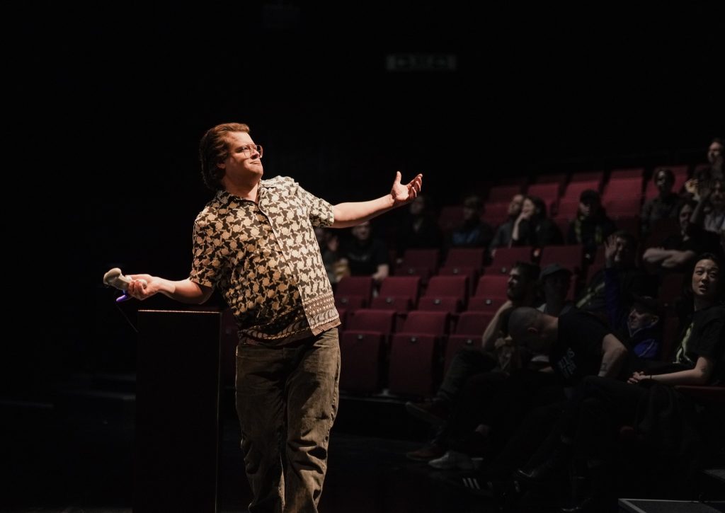 Henkilö seisoo yleisön edessä kädet levitettynä.