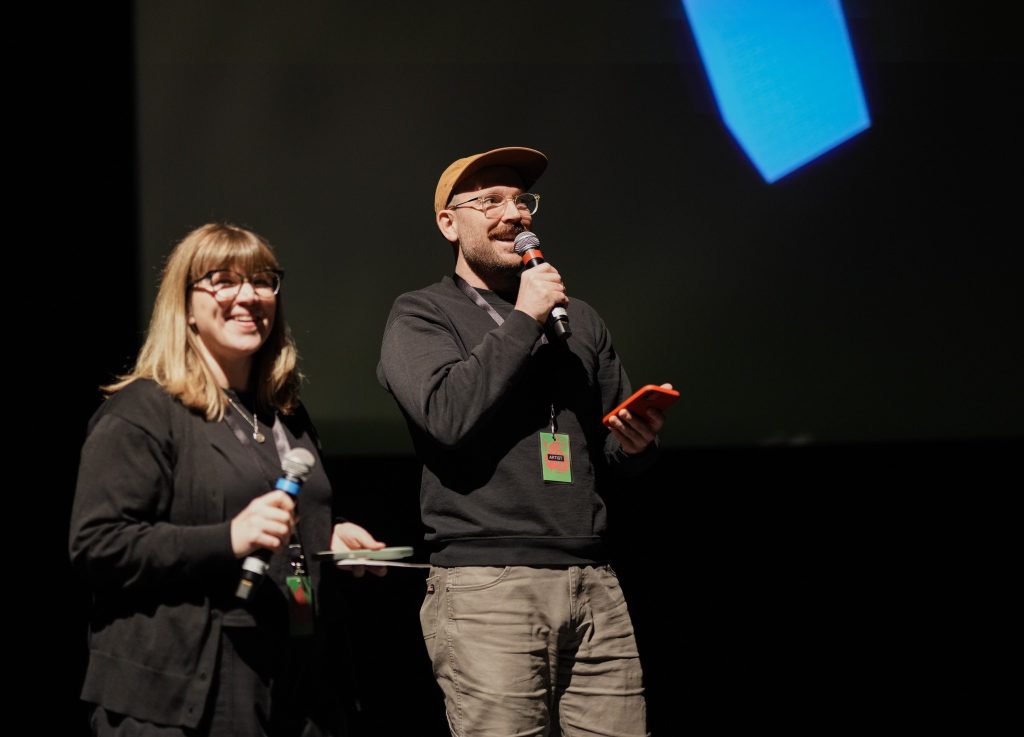 Kaksi henkilö pitelee mikrofoneja lavalla.